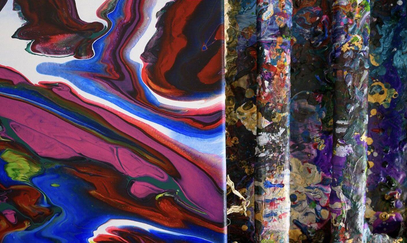 Close-up of a colorful abstract painting with swirling red, blue, purple, and green patterns on the left, beside paint-splattered wooden sticks and a textured background on the right at Greenway Lane Art Studio.