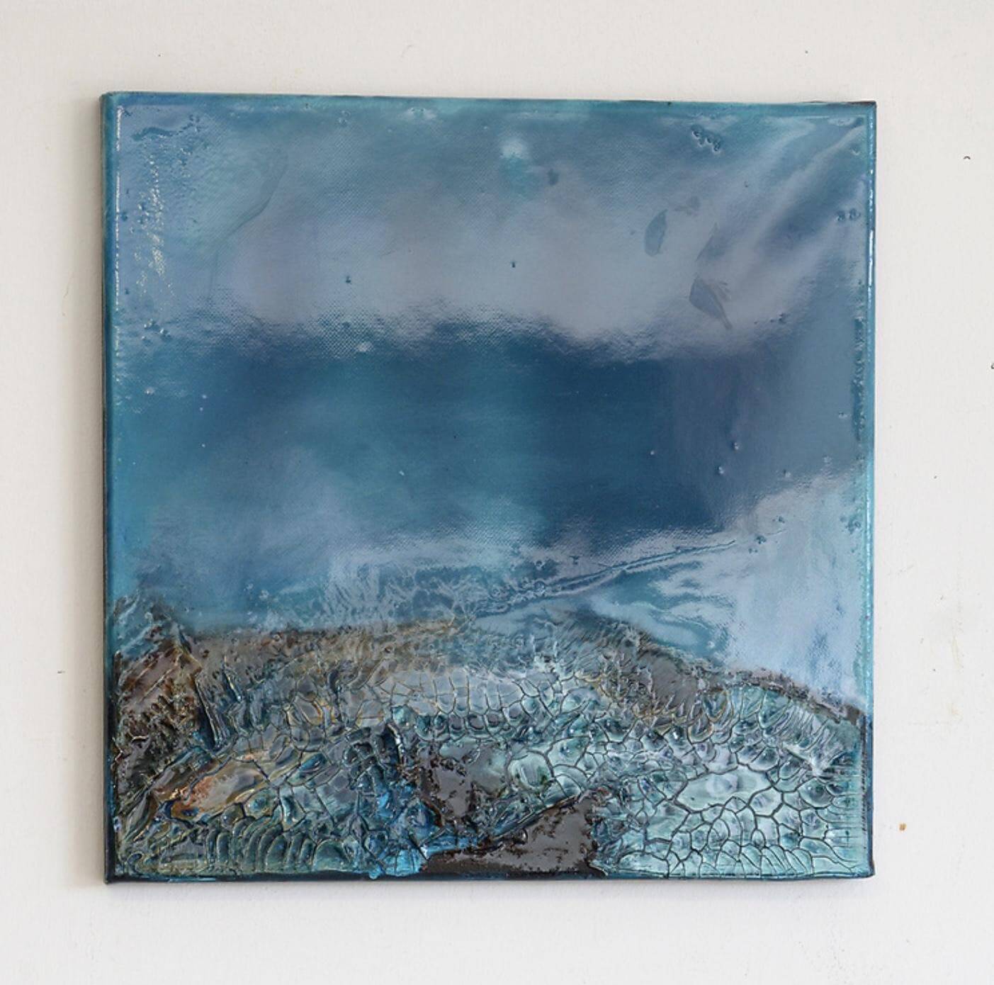 An abstract painting from Greenway Lane Art Studio featuring glossy blue and turquoise tones resembling water and sky, with textured, cracked patterns at the bottom that evoke a shoreline or tidal pool.